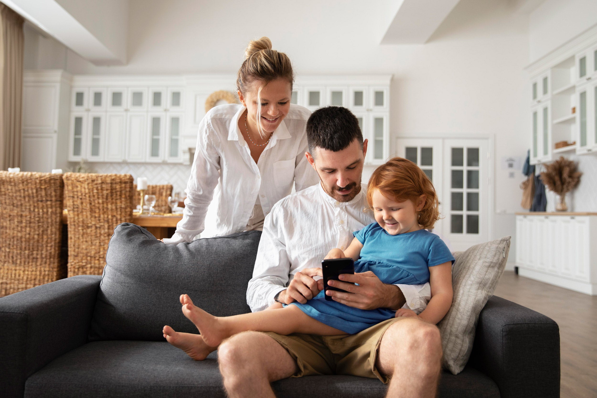 Family-dad-with-woman-and-kid-using-mobile-device-on-couch-to-arm-system