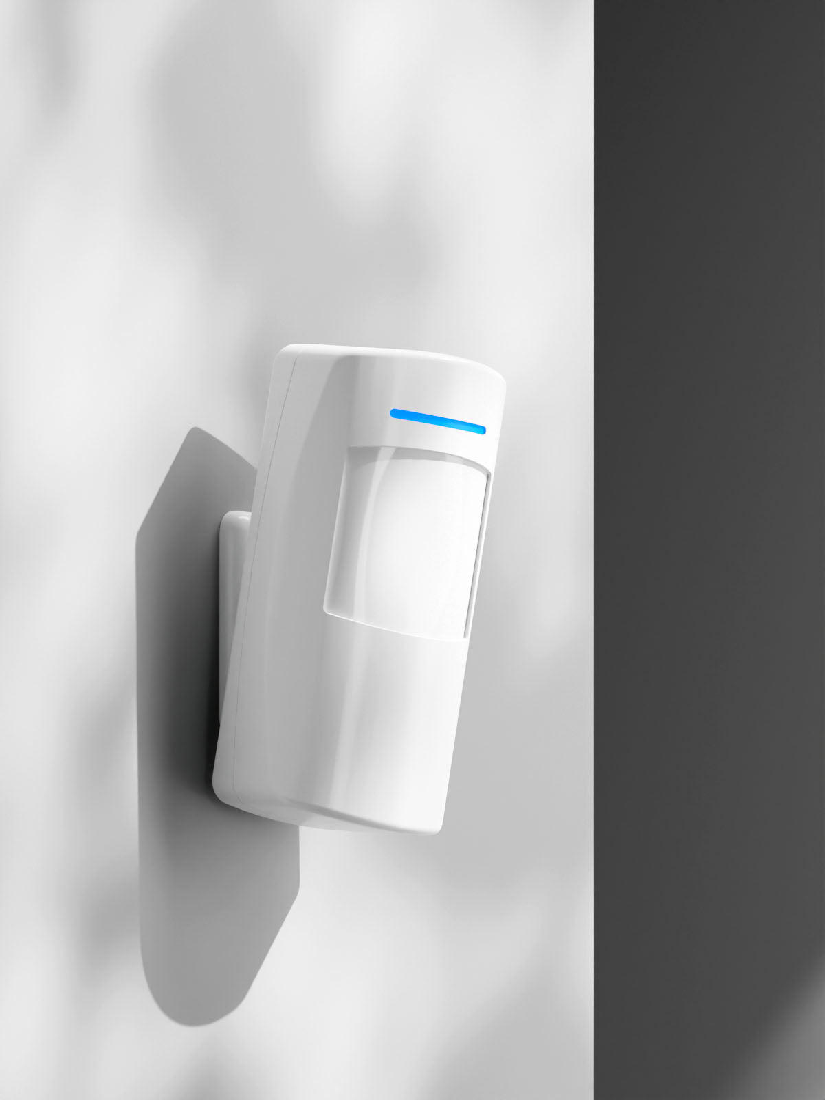 PIR Motion Sensor positioned on white smooth wall looking towards the right, with soft overlay outdoor shadows