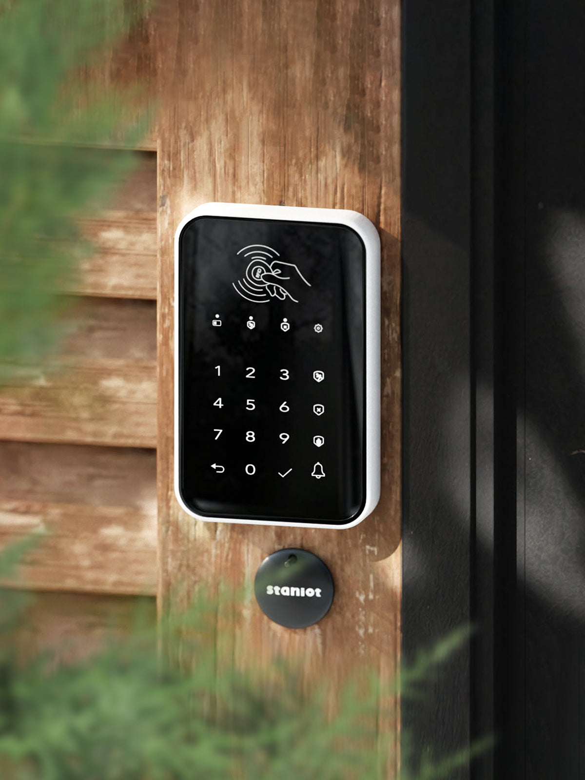 Staniot K010, RFID Wireless Alarm Touch Pad near home door entry with green vegetation on the far left